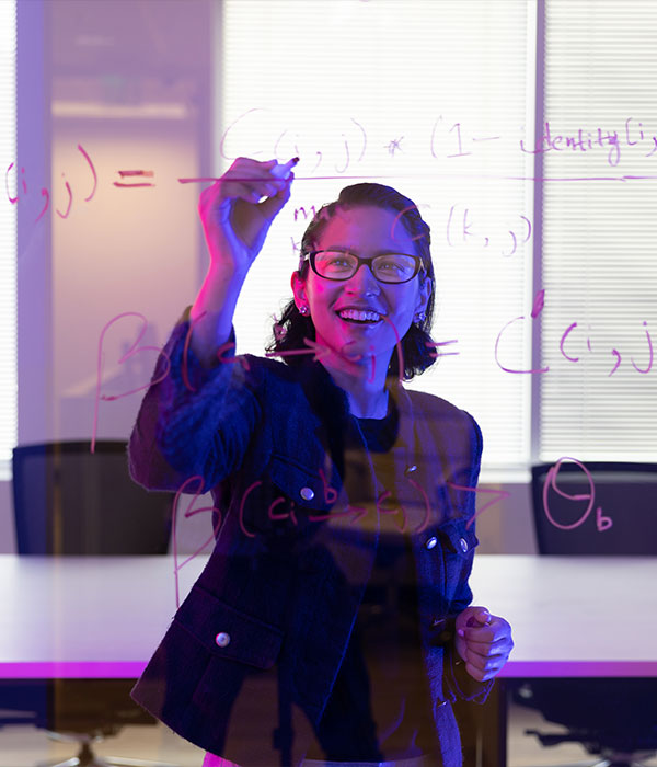 Sudhashree Sayenju writing a equation on a glass wall with a expo marker.