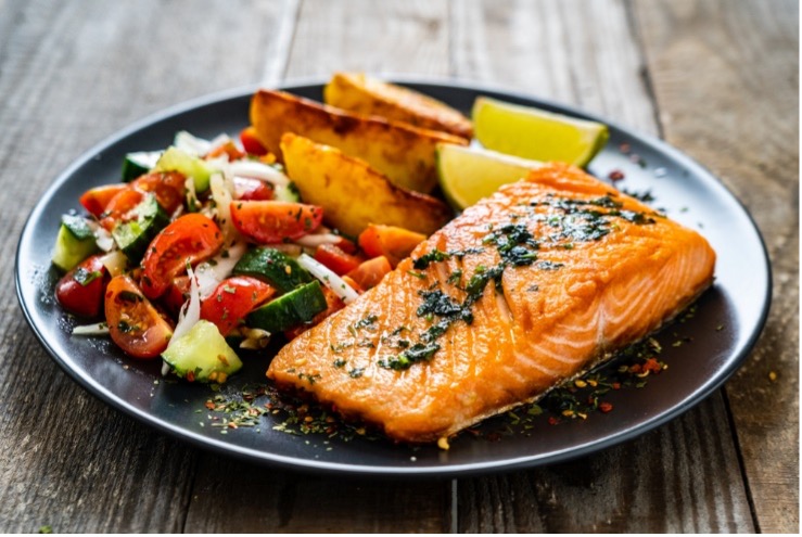 A plate of food with salmon, vegetables and fruit.