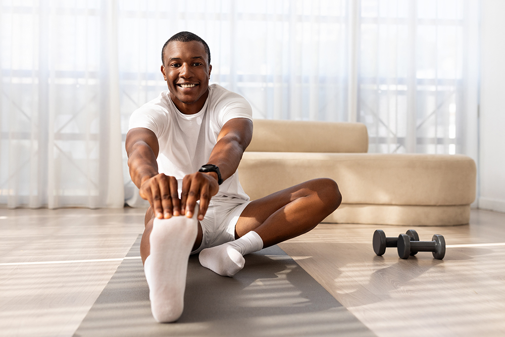 Man in workout clothes streatching out one leg with weights on the floor