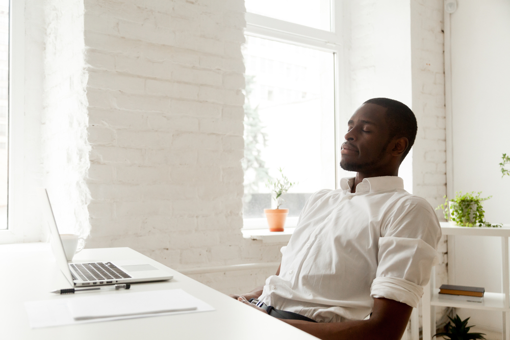man at desk with laptop open closing his eyes and reflecting