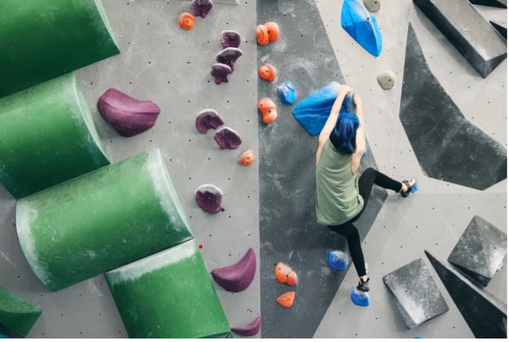 A woman holding onto a blue rock while participating in indoor rock climbing.