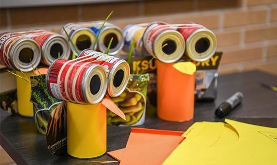 A table with owls sitting on it, that were created using cans and paper.