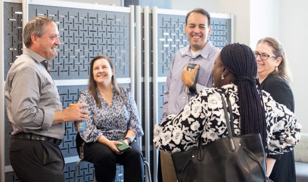 A group of five professionals engaged in a friendly conversation in an office setting.