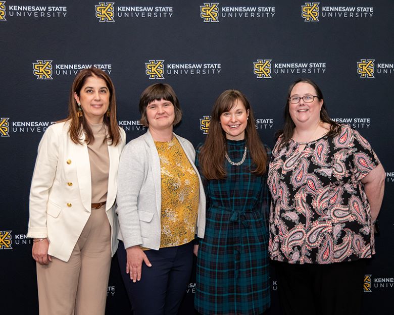 Four women standing in front of a black backdrop with the KSU logo