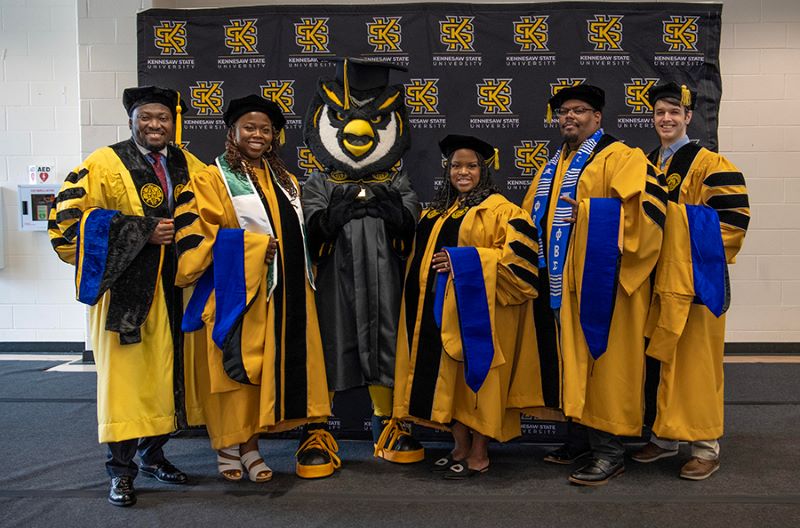KSU graduates wearing cap and gowns, standing with Scrappy the Owl