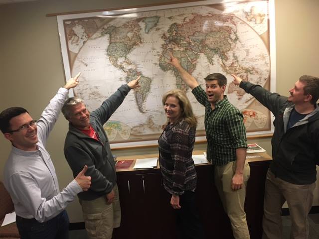 Five people smiling and pointing to a map.