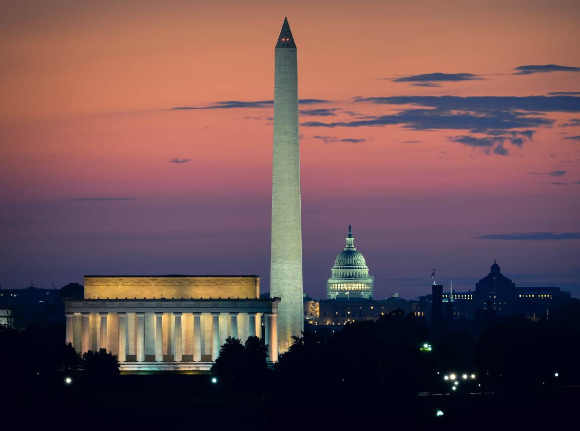 Washington, D.C. skyline at sunset featuring the Lincoln Memorial, Washington Monument, and U.S. Capitol building against a pink and purple sky.