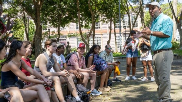 Group of students sitting outdoors listening to a tour guide.