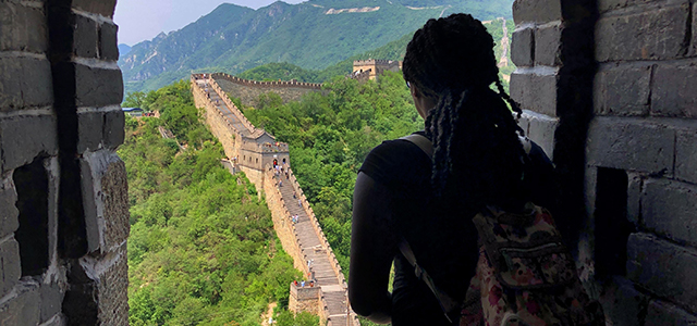 female student with backpack in archway looking out toward a stretch of the Great Wall of China