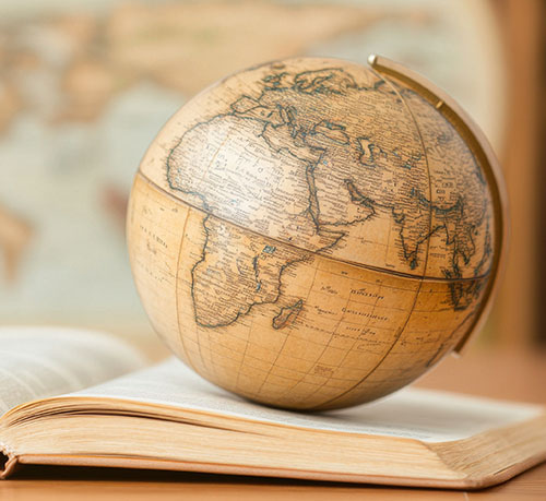 An open book supports a globe, representing the fusion of geography and education in a scholarly context.