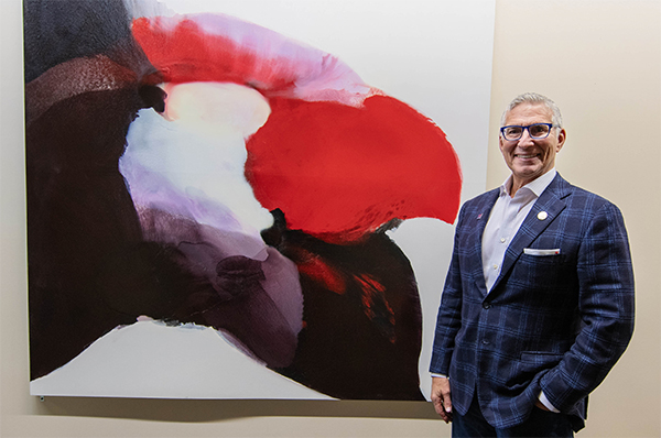 Norman Radow Poses in Front of One of His Donated Works of Art.