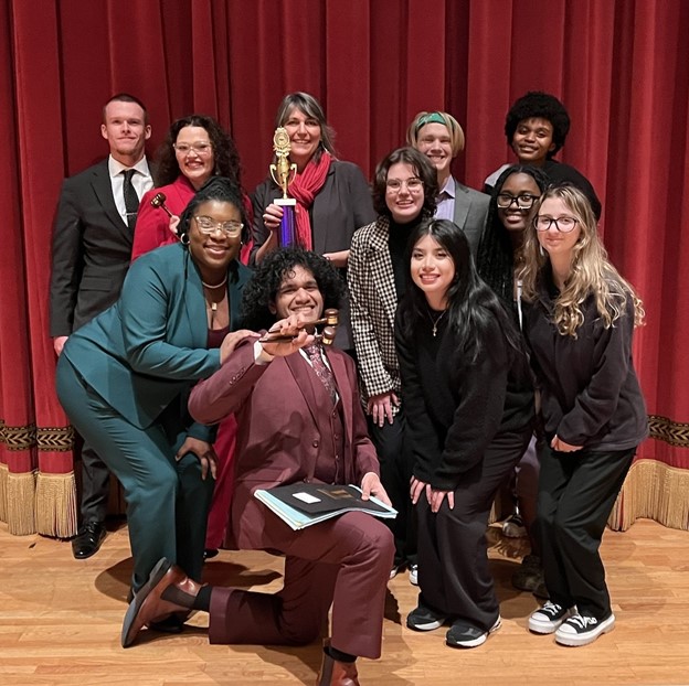 The 2023-2024 Academic Year Mocking Owls pose for a photo with their advisor and Professor of Political Science Elizabeth Gordon, Ph.D., (holding trophy) in celebration of a successful mock trial competition.