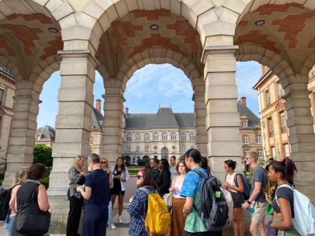 Students gather in front of a historic building featuring elegant arches, capturing a moment of exploration and admiration.