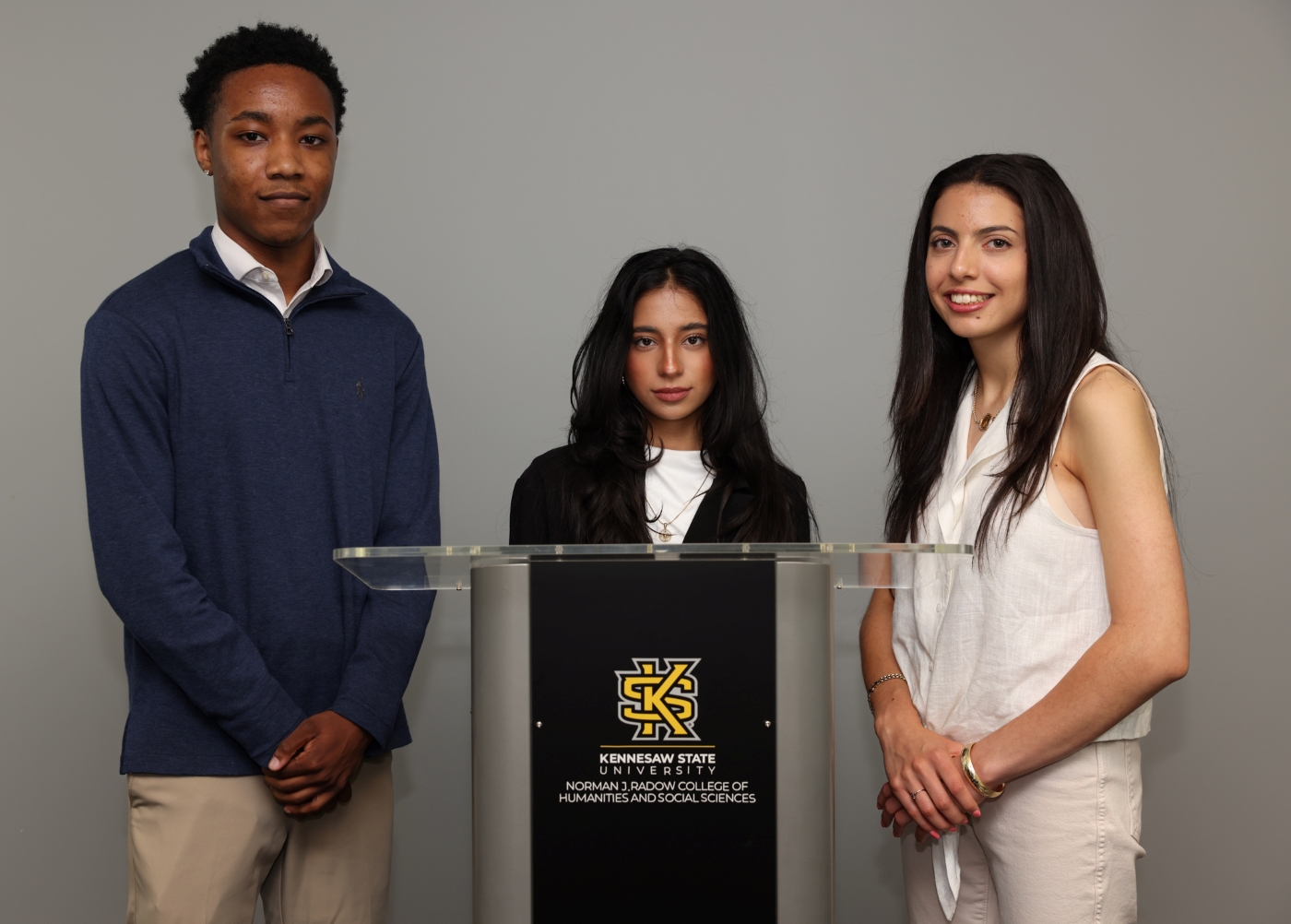 KSU students Jaylan Conwell, Zainab Wajid, and Silvia Prisco stand around a podium with Kennesaw State logo