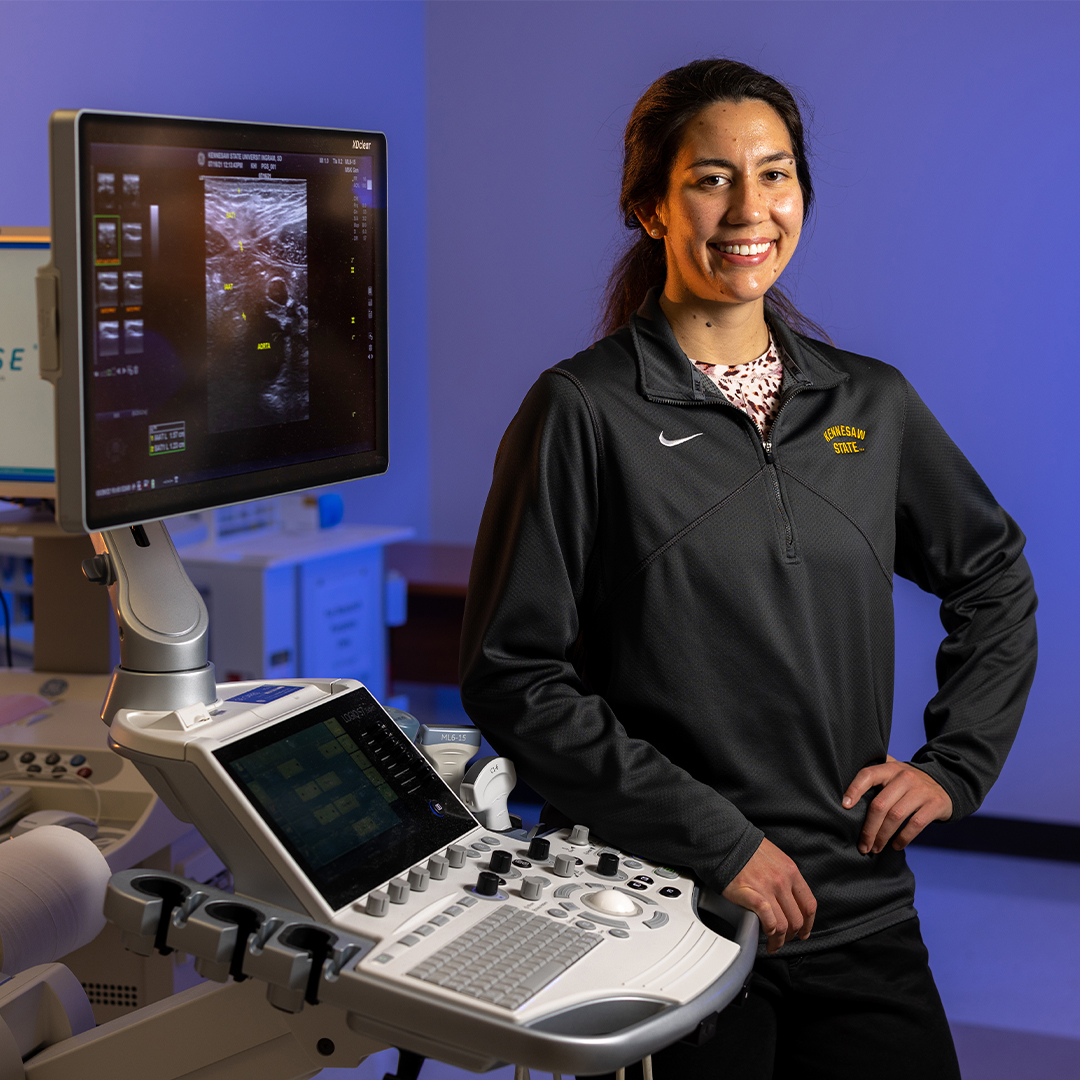 ksu graduate female studio smiling in front of medical equipment