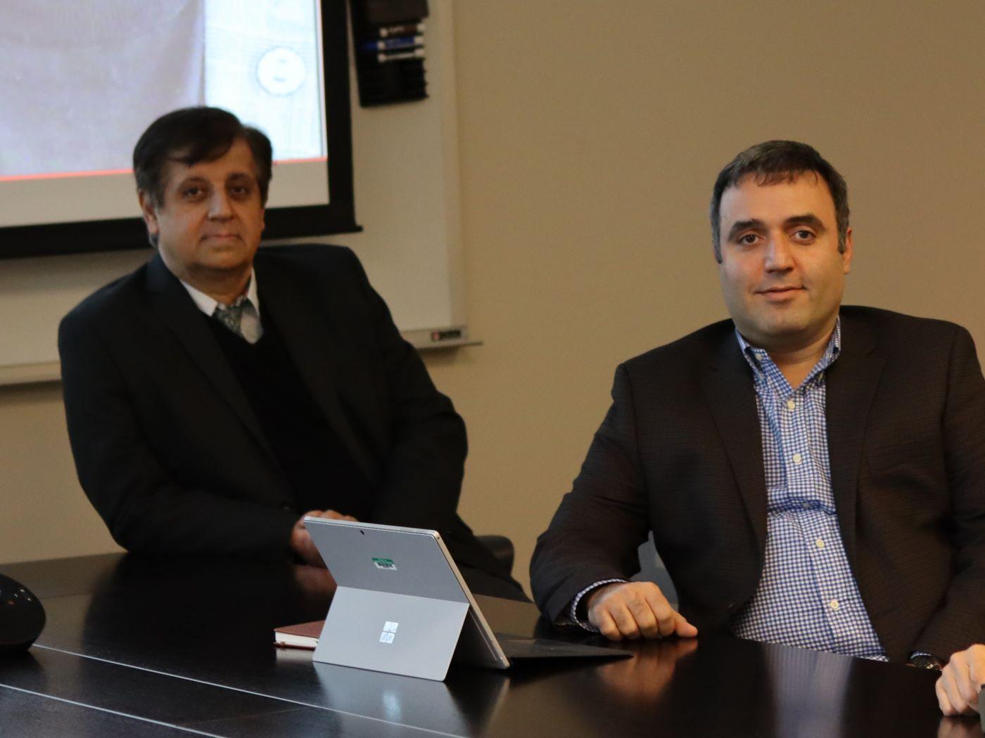 Two men sitting at a table with a laptop in an office setting / 