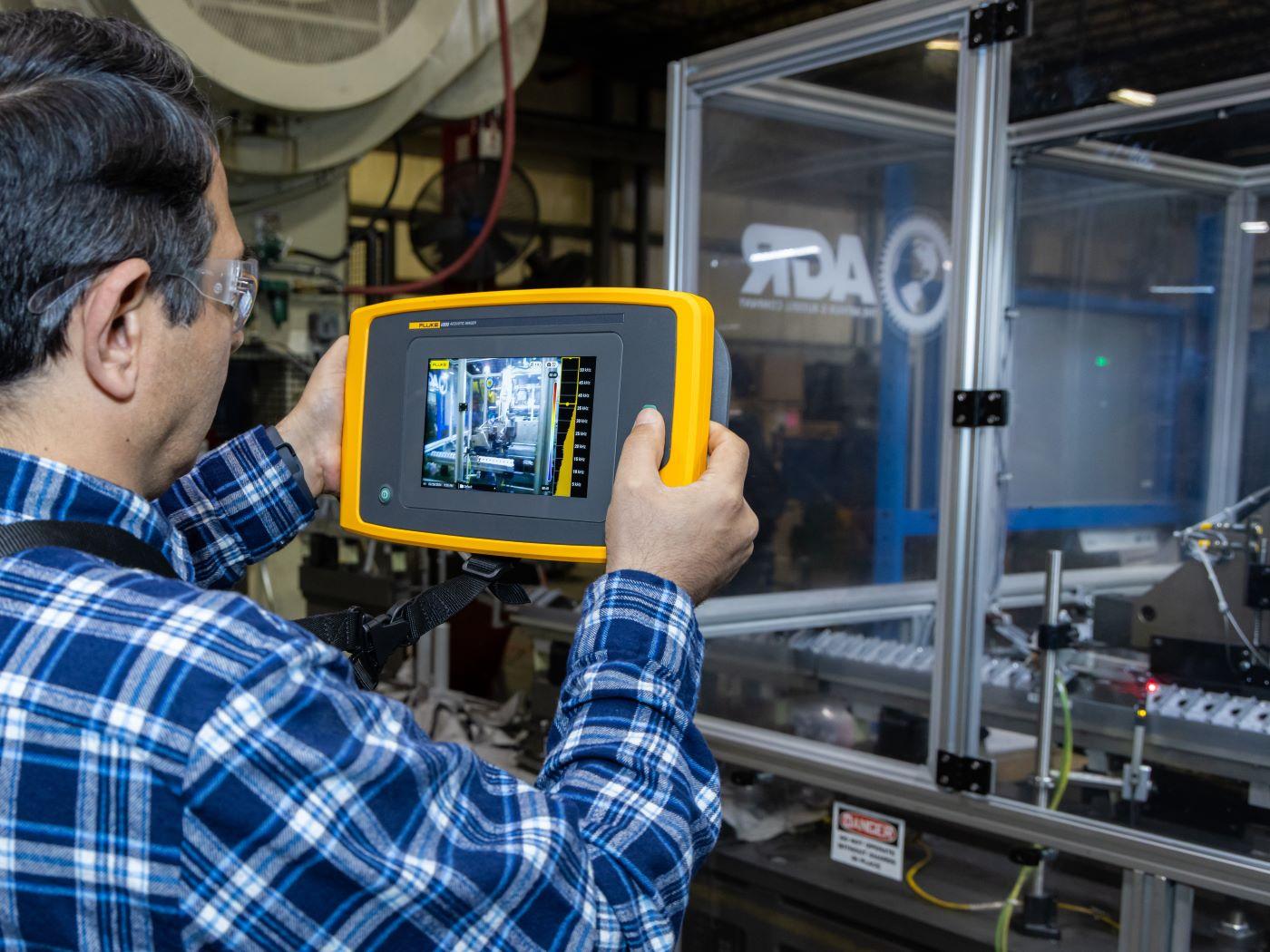 Person holding a yellow and black diagnostic device showing machinery on its screen. / 