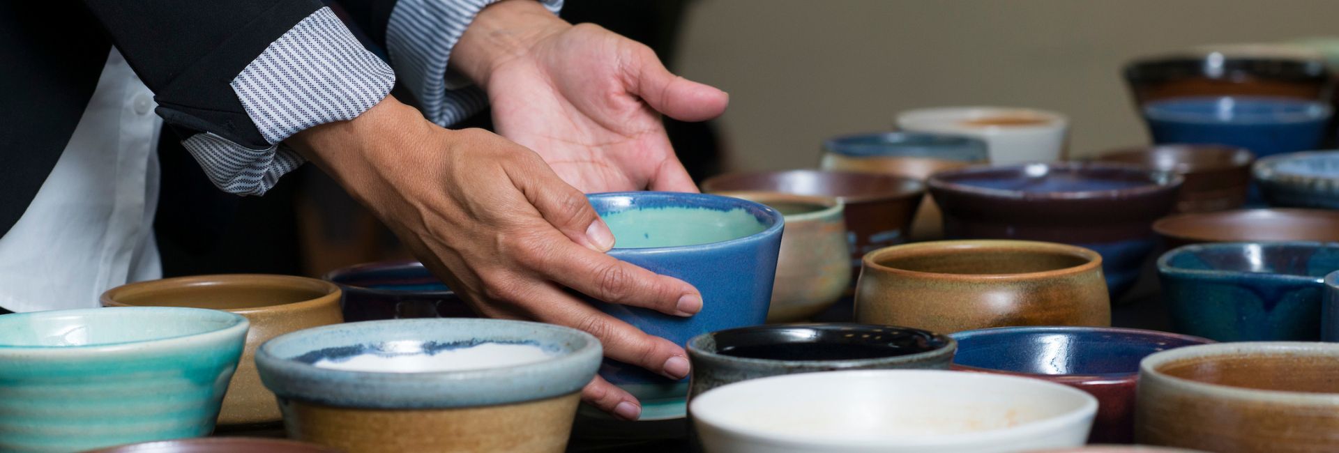 A table full of empty bowls with a student adding another empty bowl to it.