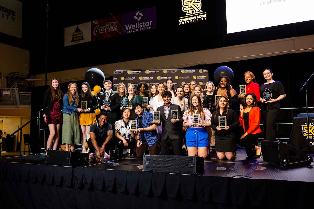 All of the student leader award winners pose for a photo with their awards on stage.