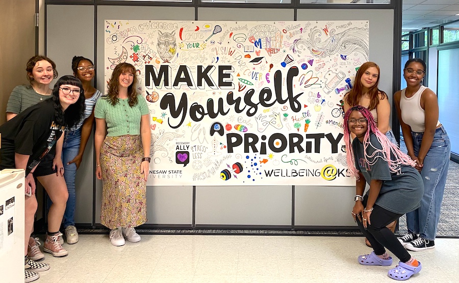 Peer counselors posing with an art mural that says make yourself a priority