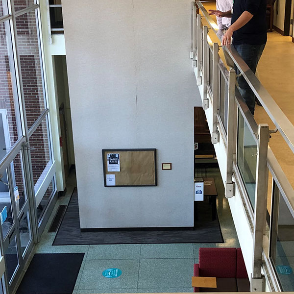 Interior of student center with people looking over balcony through tall windows out to court yard and old interior wall center.