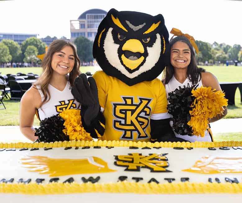 cheerleaders with scrappy standing in front of cake