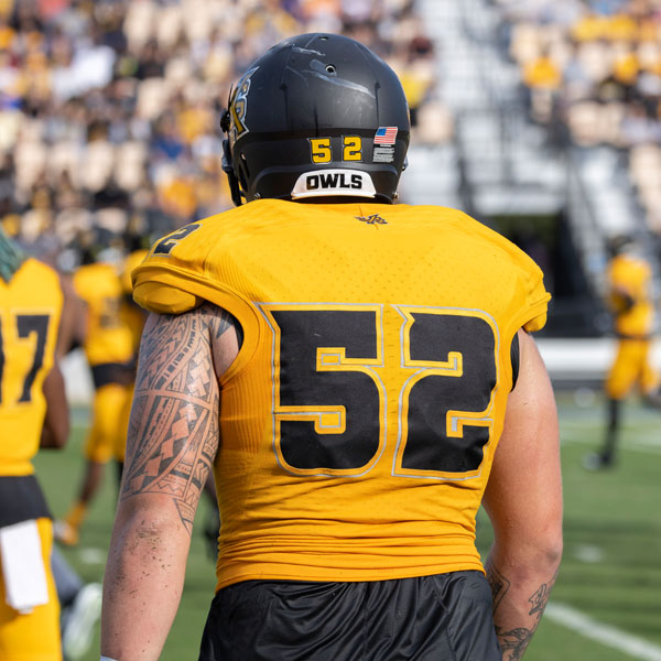 ksu football player standing on field with back turned =  number 52 in black and gold on the back of a football player on the field