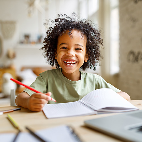 young boy with curly hair and red pencil smiling