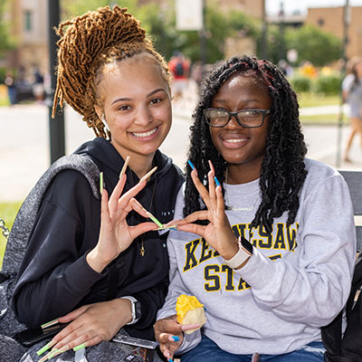 two girls on campus giving the owl sign