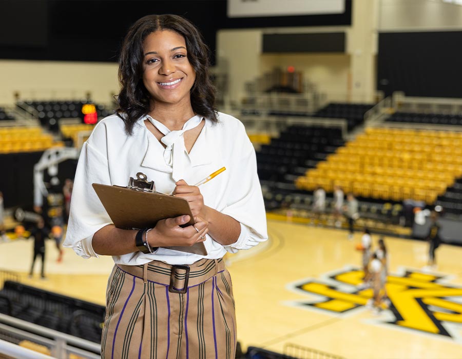ksu student holding a clipboard in the basketball gym.