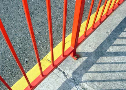 edge of an orange fence casts a shadow on the sidewalk. Image is titled “lines” by Charlotte Kinzie 